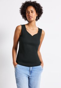 Czarny bezrękawnik z dekoltem w kształcie litery V, wykonany z prążkowanego materiału. Połączony z jasnoniebieskimi dżinsami z widocznymi detalami guzików.