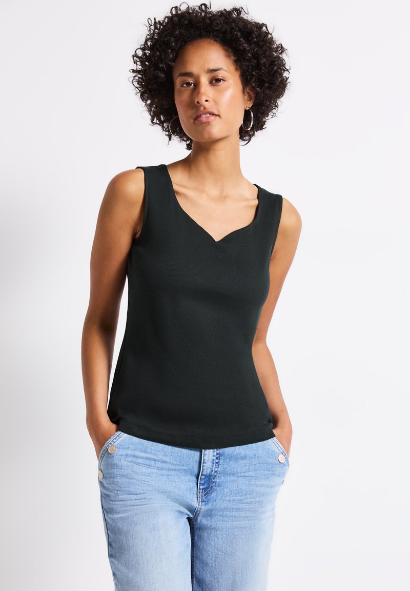 Czarny bezrękawnik z dekoltem w kształcie litery V, wykonany z prążkowanego materiału. Połączony z jasnoniebieskimi dżinsami z widocznymi detalami guzików.