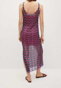 Robe de couverture tricotée avec un motif en chevrons dans des teintes vives de rose, violet et vert, sans manches et avec des fentes sur les côtés pour faciliter les mouvements.