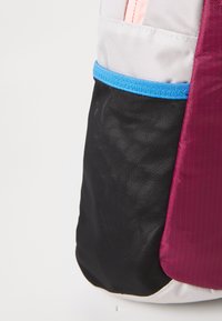 Mochila multicolorida com um fundo em malha preta, um lado em vinho, uma parte superior cinza e uma faixa de destaque azul. Tecido liso e durável.