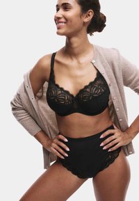 Sort blonde-bh med bølget kant og matchende højtaljede trusser, lagdelt under en beige cardigan. Glat tekstur, detaljeret mønster.