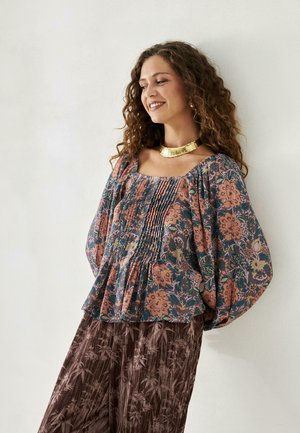 Blusa fluida con estampado floral oscuro y acentos en durazno y verde, que presenta un escote cuadrado y detalles plisados. Combinada con pantalones oscuros con estampado.