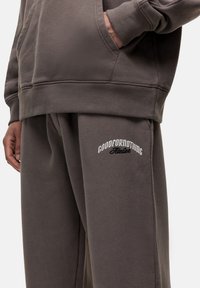 Grauer Hoodie mit einer Fronttasche und gerippten Bündchen, kombiniert mit passender Jogginghose, die das gestickte Logo "GOODFORNOTHING" trägt. Weicher Stoff.