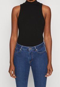 Bodysuit negro de canalé sin mangas con un cuello alto, combinado con unos vaqueros de denim azul que presentan un cierre de botón y detalles de costura sutiles.