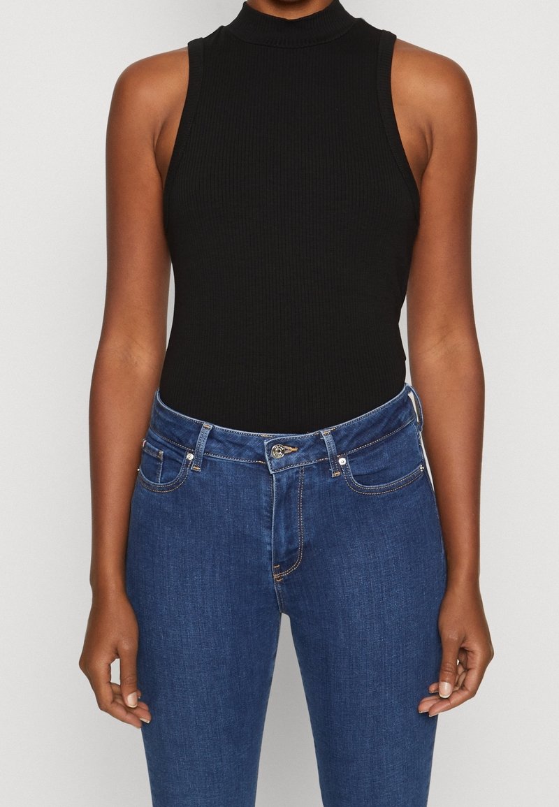 Bodysuit negro de canalé sin mangas con un cuello alto, combinado con unos vaqueros de denim azul que presentan un cierre de botón y detalles de costura sutiles.