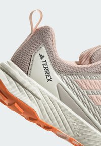 Lightweight athletic shoe featuring a textured pink mesh upper, gray accents, a rubber sole with orange traction, and branding on the side.