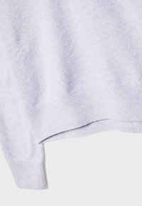 Close-up of light gray knit sweater showing ribbed sleeve cuff and ribbed hem detail.