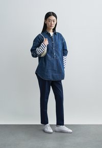 Denim shirt with a button-up front, long sleeves featuring navy and white stripes, paired with navy trousers and white sneakers.