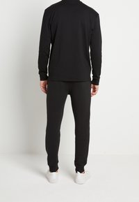 Zwart set met lange mouwen en broek, gemaakt van zachte stof. Getailleerd ontwerp met ribbelmanchetten, gecombineerd met witte sneakers. Eenvoudig, effen kleur.