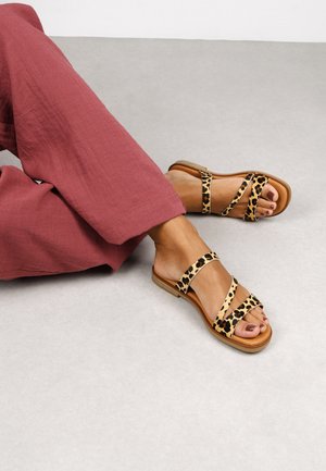Sandalias planas de estampado de leopardo con tiras cruzadas y una base marrón claro, combinadas con pantalones burdeos holgados.