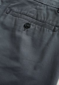 Pantalon en tissu gris foncé avec une poche arrière boutonnée et des coutures visibles sur un matériau lisse.