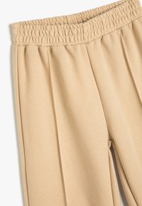 Beige joggerbroeken met een elastische tailleband, zachte textuur en geplooide details. De stof lijkt glad en casual in ontwerp.