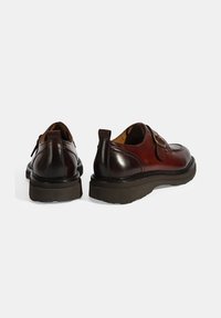 Braune Lederschuhe mit einem runden Zehen-Design, Schnallendetail und einer dicken schwarzen Gummisohle mit strukturiertem Grip.