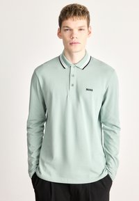 Polo de manga comprida em algodão verde menta com gola riscada preta e branca, apresentando um pequeno logo preto "BOSS" no peito.