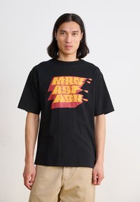 Black cotton t-shirt featuring a large yellow and red graphic print with a dripping effect, short sleeves, and a relaxed fit.