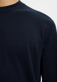 Granatowa, bawełniana bluzka z długim rękawem, z okrągłym dekoltem, gładką fakturą i minimalnymi detalami szwów. Prosty i klasyczny design.