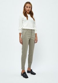 Maglione leggero e aderente color crema abbinato a pantaloni tapered color khaki chiaro; i pantaloni presentano tasche laterali e una leggera fessura all'orlo. Scarpe nere con tacco blocco.
