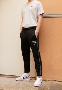 Grå Nike T-shirt med svart logotyp, ihop med svarta Nike sweatpants med vita sidostråk och en logotyp, avslutat med vita sneakers.