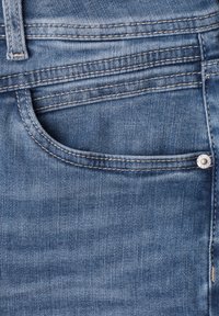 Close-up of blue denim jeans front pocket with visible stitching, belt loop, and metal rivet on the right side.