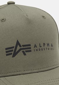 Zöldes-négyzetes sapka, texturált anyagból készült, elöl fekete logóval, geometrikus mintával és az "ALPHA INDUSTRIES" felirattal.