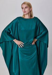 Robe en satin bleu-vert avec de larges manches chauve-souris et un col bateau. Sa texture lisse et son drapé élégant forment une silhouette fluide.