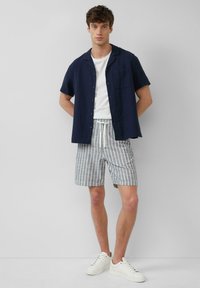 Marineblauwe korte mouwen shirt, witte T-shirt, grijs gestreepte shorts met koord, en witte sneakers. Eenvoudig ontwerp en ademend materiaal.
