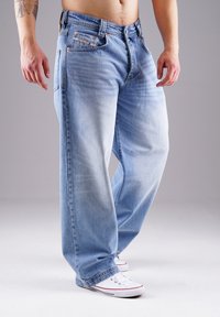 Hellblaue Jeans im entspannten Schnitt, mit fünf Taschen, Metallbeschlägen und dezentem Verblassen. Getragen mit weißen Sneakern.