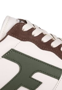 White leather sneaker with brown suede accents, featuring green logo detail, cream laces, and textured surface for grip.