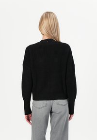 Schwarzer, gestrickter Pullover mit strukturierter Oberfläche, abfallenden Schultern und rundem Halsausschnitt. Verfügt über eine kleine Öffnung im Rücken mit einem Knopf.