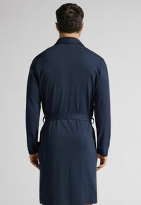 Námořnický župan s dlouhými rukávy, nastavitelným páskem v pase a hladkým povrchem, s klasickým límcem a designem s otevřeným zadním dílem.