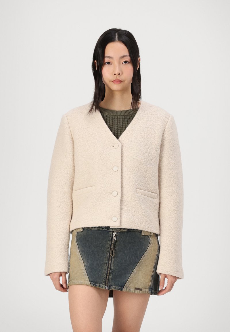 Giacca beige, strutturata, corta con scollo a V, bottoni frontali e tasche laterali, abbinata a una gonna in denim multicolore con zip.