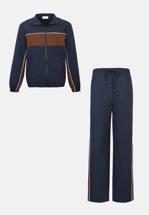 Marineblaue und braune Trainingsanzug mit durchgehendem Reißverschluss an der Jacke, die Reißverschlusstaschen besitzt, und passenden Hosen mit Kordelzug und seitlichen Streifen.