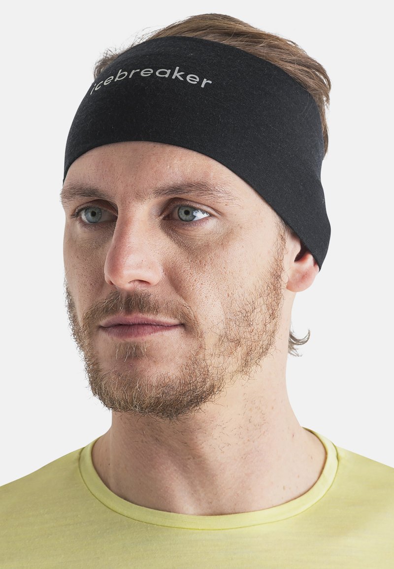 Mężczyzna z jasną brodą, noszący czarną opaskę na głowę "Icebreaker" i jasną żółtą koszulkę z okrągłym dekoltem, zwrócony nieco w prawo na jednolitym białym tle.