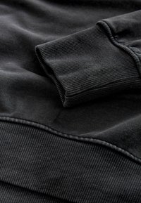 Czarna bluza z ribbowymi mankietami i dołem, o gładkiej fakturze. Materiał prezentuje delikatne różnice w odcieniach.