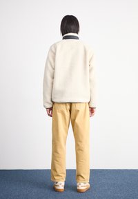 Jachetă din fleece de culoare crem cu guler negru, asortată cu pantaloni bej și adidași albi. Textură netedă și croială lejeră.