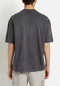 Camiseta gris oversized de algodón, con mangas cortas, cuello de canalé y una textura suave con un ajuste relajado.