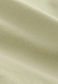 Tissu vert pâle avec une surface lisse et texturée, présentant un motif de tissage subtil. Matériau doux et flexible avec une couleur uniforme.