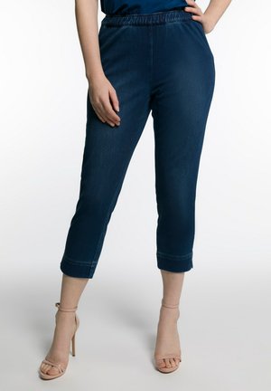 Pantalons en denim bleu foncé, coupés, avec une taille élastique. Texture lisse, design à jambes droites et ourlets retroussés. Associés à des talons hauts nude.