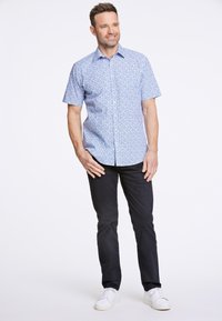 Camicia a maniche corte, con bottoni, di colore azzurro chiaro con un motivo floreale. Indossata con pantaloni scuri e sneaker bianche. Tessuto morbido e vestibilità su misura.