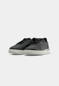 Paire de baskets basses en cuir noir avec semelles blanches et lacets noirs, affichant le logo BOSS sur le côté, placées sur fond blanc.
