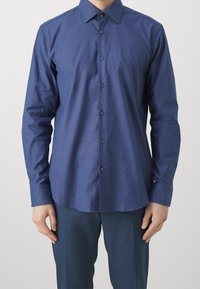 Tmavě modrá košile na knoflíky s texturovanou látkou, límcem s rozloženými klopy a knoflíky v barvě košile, doplněná o tmavě modré kalhoty na míru.