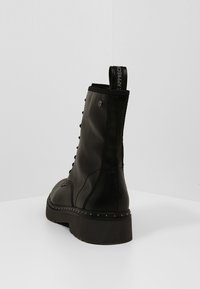 Zwarte leren enkelboot met een vetersluiting, middenzool versierd met studs en een lus aan de achterkant voor gemakkelijk aan- en uittrekken. Getextureerde zool.