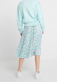 Ljusblå tröja i kombination med en plisserad, blommönstrad kjol i nyanser av rosa och lila. Mjuk tyg med en svävande silhuett. Vita sneakers.