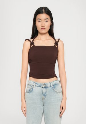 Bruine nauwsluitende tanktop met vierkante hals en geraffineerde zijkanten, voorzien van lusvormige schouderbanden. Gecombineerd met lichtblauwe hoge taille jeans.