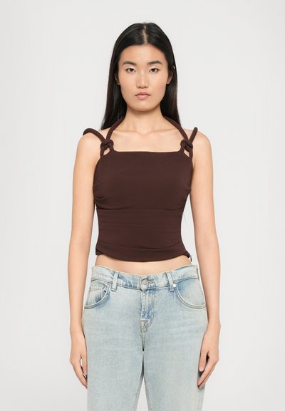 Débardeur marron ajusté avec encolure carrée et côtés froncés, doté de bretelles en boucle. Assorti avec un jean taille haute bleu clair.