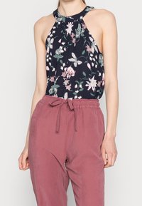Blommig halterneck-topp med en mörk marin bakgrund, prydd med rosa och gröna mönster, i kombination med lösa byxor i dammig ros med knytband i midjan.