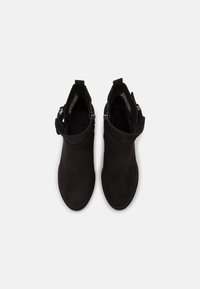 Botines de ante negros con textura suave, cierre de cremallera y un diseño de puño ligeramente acampanado en la parte superior. Suelas planas.