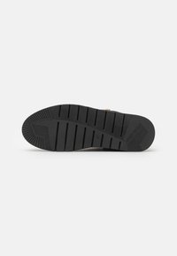 Semelle de chaussure noire avec des rainures profondes et des motifs texturés pour une bonne adhérence, présentée sur un fond blanc uni.