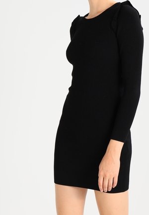 Robe-sweater noire à côtes avec manches longues, silhouette ajustée et détails en volants au niveau des coutures des épaules, fabriquée en tissu tricoté.