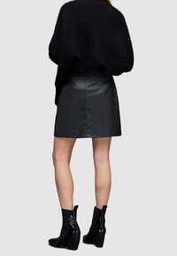 Černá kožená minisukně s přiléhavým střihem, doplněná černými kotníkovými botami na podpatku. Pozadí je neutrální šedé.